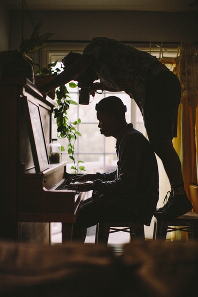 人坐而弹钢琴而其他男子站在凳子上,把人的手在钢琴在房间的照片
